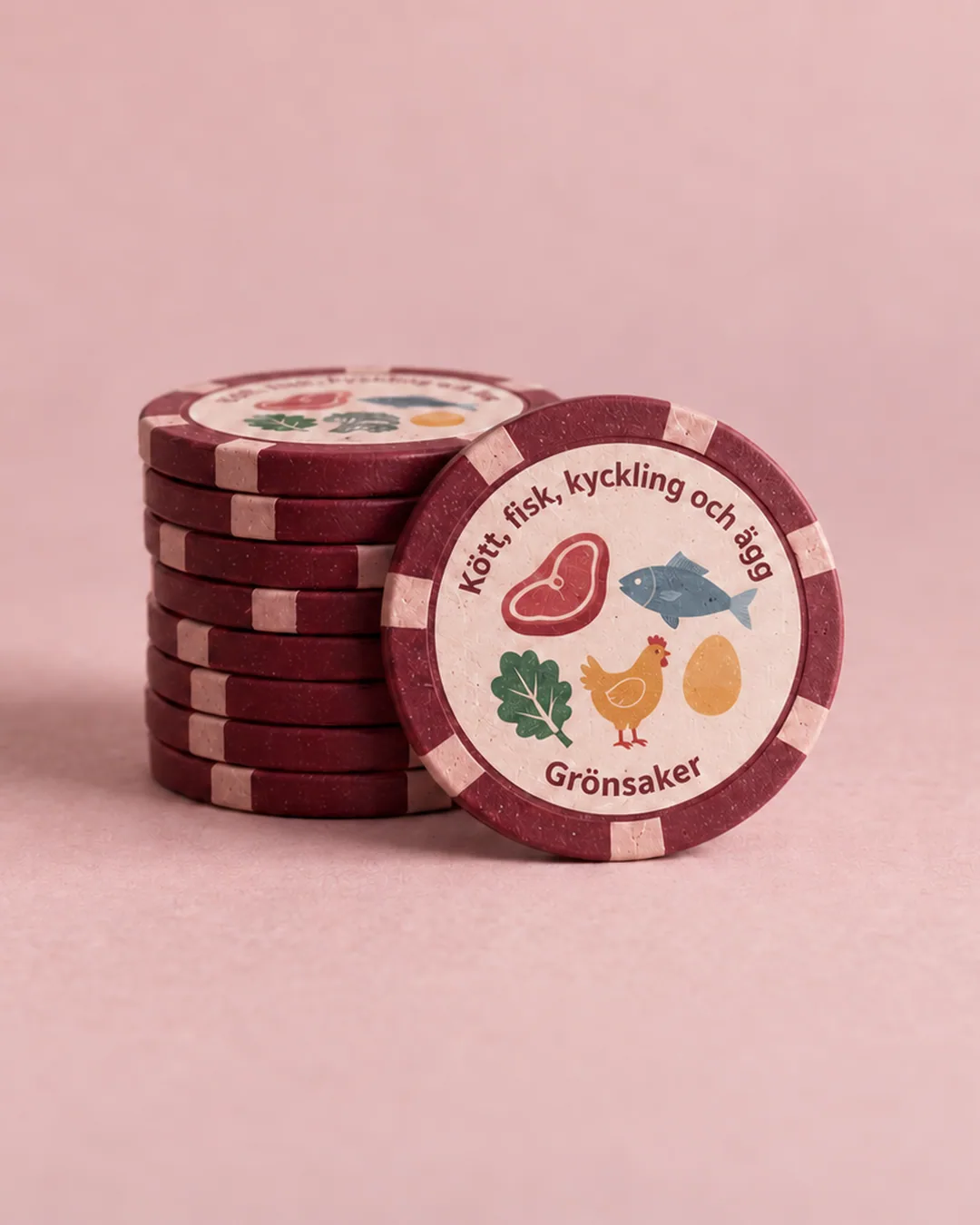 Stapel vinröda pokerchips på rosa bakgrund, där det främsta chipet visar kött, fisk, kyckling, ägg och grönsaker, symbol för All in